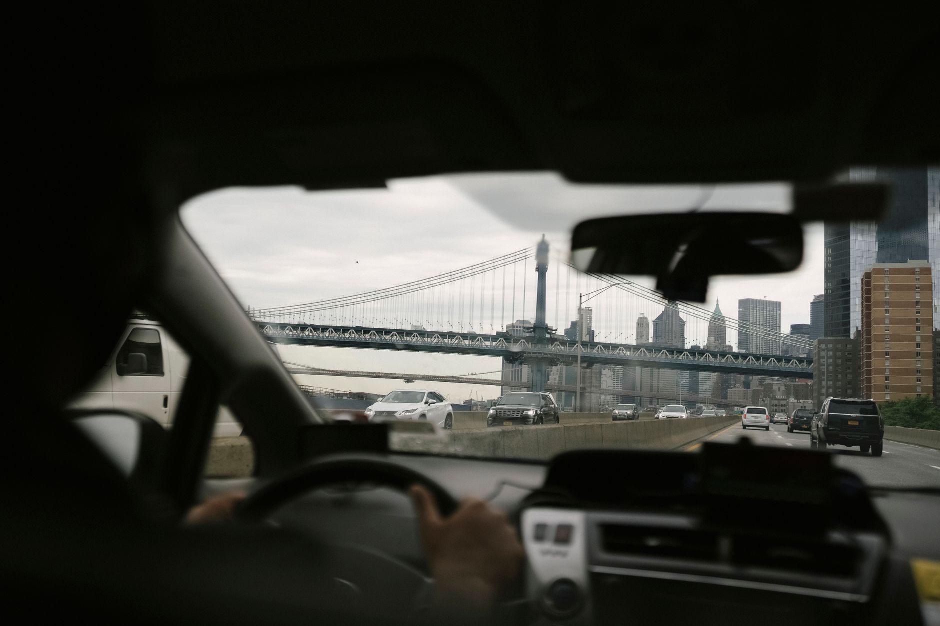 Back view of anonymous male driving car along roadway against bridge on urban background in soft daylight